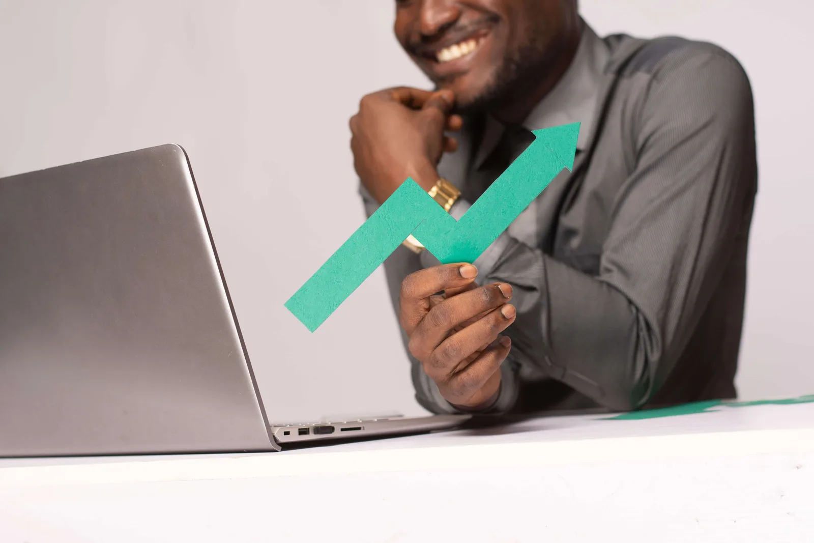 African business man holding a green graph line pointing up and smiling while looking to laptop