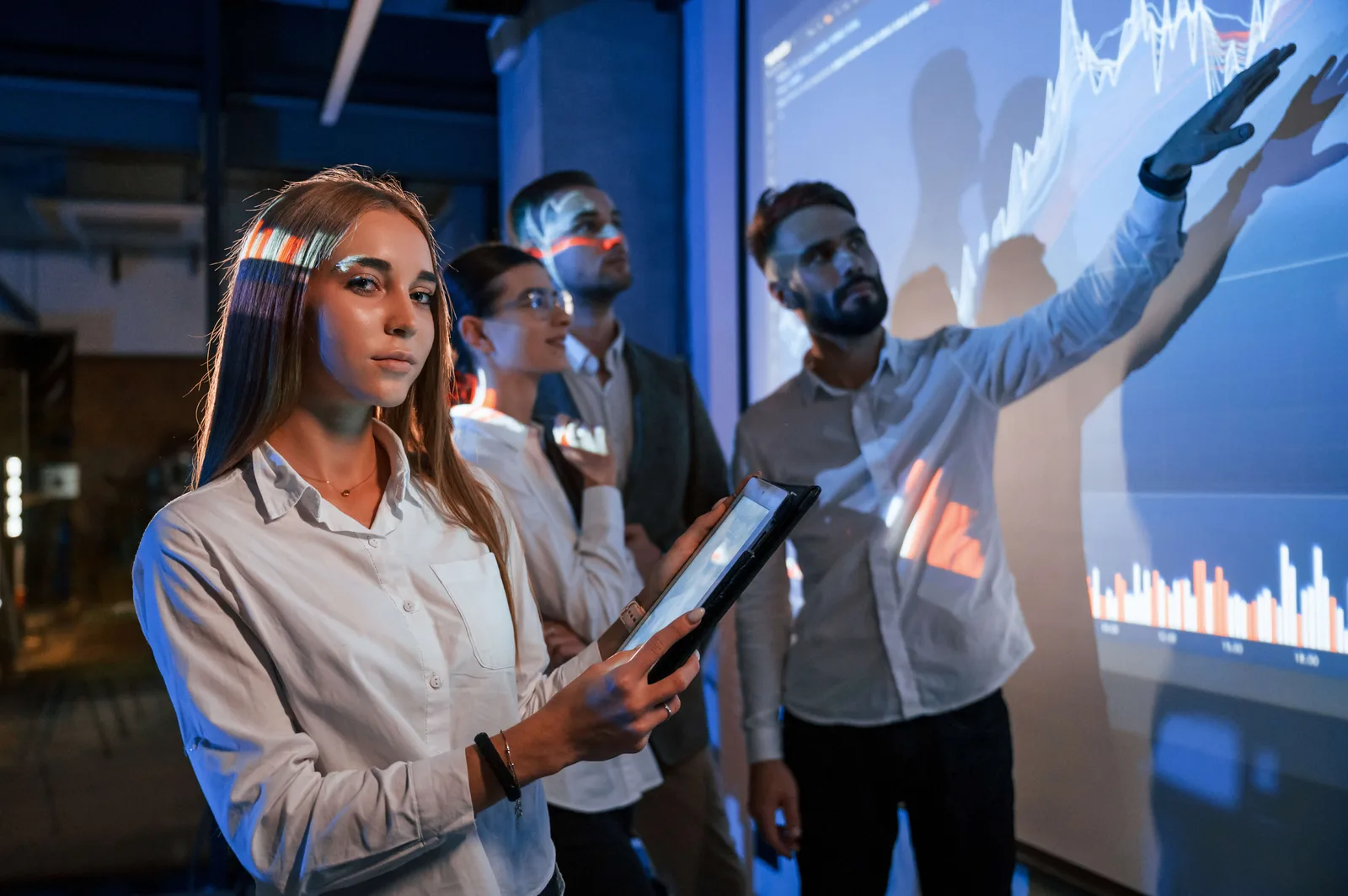 Female holding tablet. Male talking to employees, showing the positive plan on the projector in office