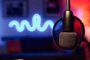 Microphone hanging in front of camera over workplace of radio presenter or podcast creator in studio illuminated with neon lights