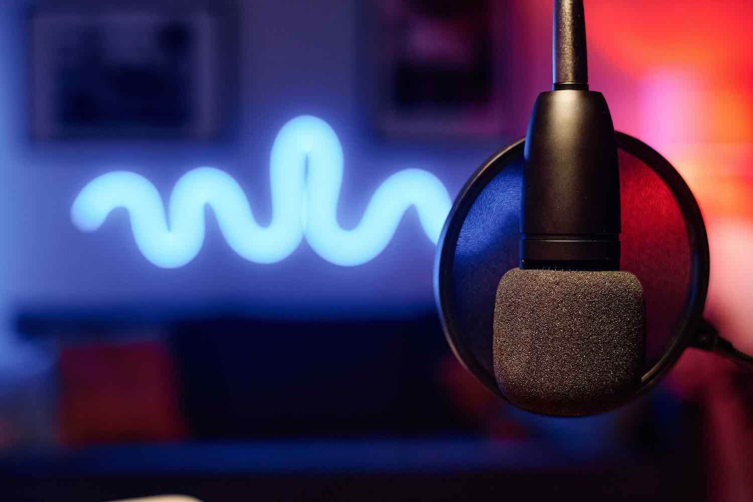 Microphone hanging in front of camera over workplace of radio presenter or podcast creator in studio illuminated with neon lights